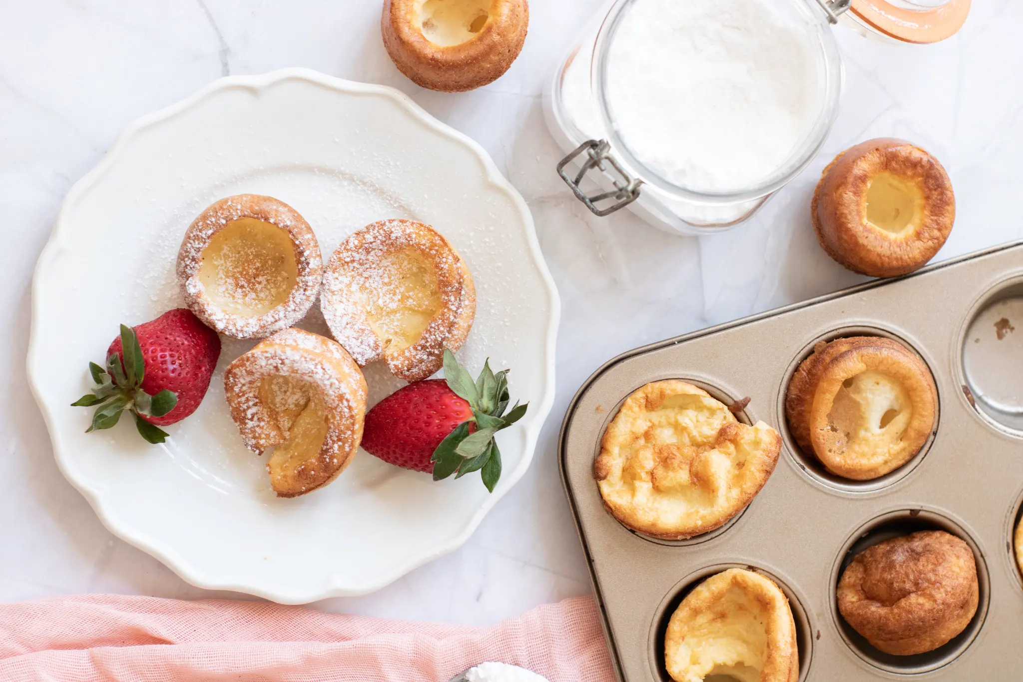 Golden popovers with strawberries beside a baking tin